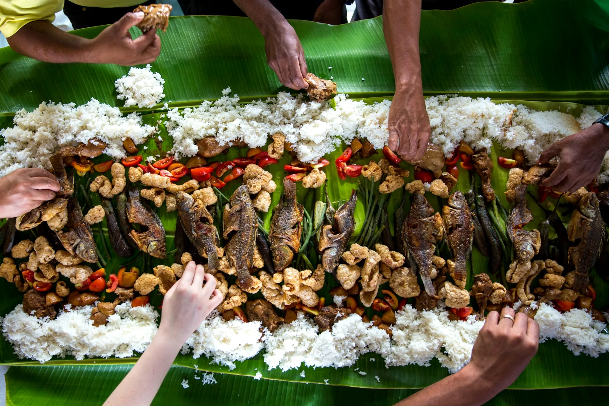 Viele Hände greifen beim philippinischen Festessen nach Reis, Fisch und Gegrilltem auf Bananenblättern